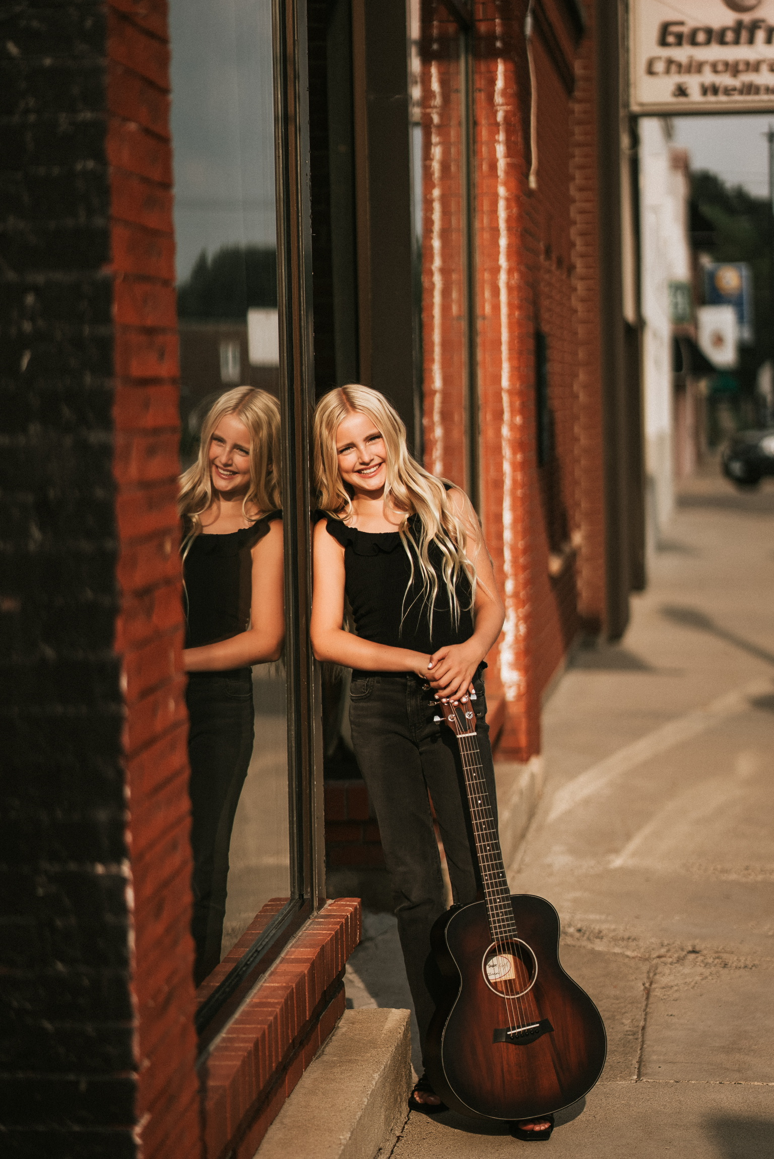 Brooklyn Marie leaning against a storefront window with her acoustic guitar